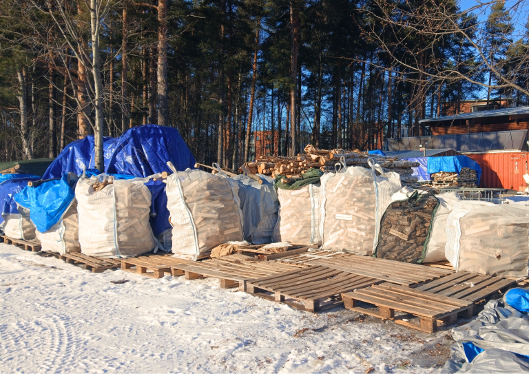 Suuria muovisäkkejä jotka ovat täynnä valmiita halkoja odottamassa ostajaansa kestävän kehityksen keskuksen pihalla.