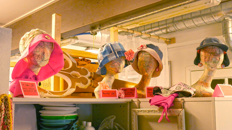Myymälähyllyjen päälle on asetettu neljä mannekiinipäätä, joiden päihin on asetettu koristeellisia hattuja myyntiin.