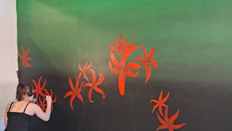Nuorten Startin vihreään sisäseinään on nuori nainen maalaamassa punaisia kukkia.