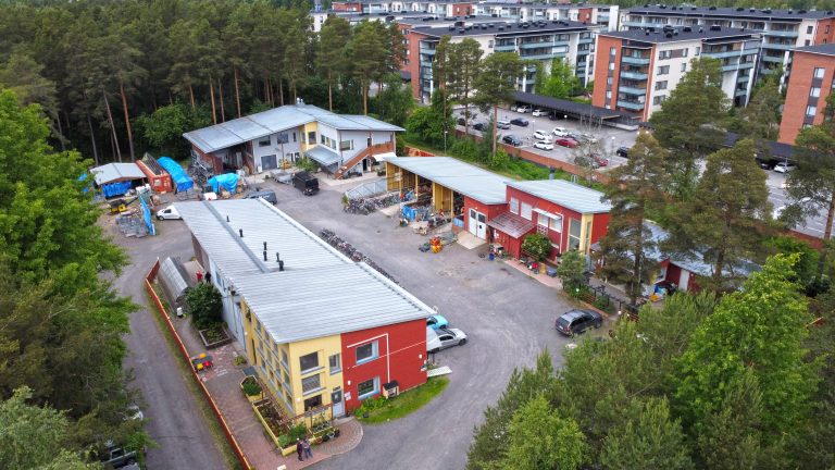 Kestävän kehityksen keskuksen Sorvi-toimipaikan piha ilmasta katsottuna. Pihalla on kolme eriväristä rakennusta, useita autoja ja lukemattomia polkupyöriä.