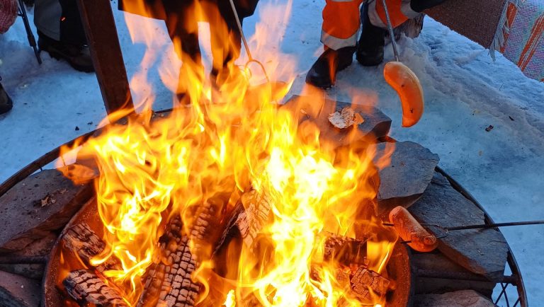 Joukko kekeläisiä roihuavan nuotion ympärillä paistamassa makkaraa.