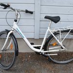 Valkoinen 28-tuumainen naistenpyörä. Pyörässä näkyy seisontatuki, useita heijastimia, tarakka, käsijarru ja soittokello.