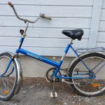 Sininen 24-tuumainen Kombi Maxi merkkinen, matalarunkoinen kaupunkipyörä. Pyörässä näkyy useita heijastimia, seisontatuki, tarakka ja soittokello.
