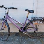 Violetti 7 vaihteinen, 28 tuumainen Nakamura merkkinen matalarunkoinen kaupunkipyörä, pyörässä on soittokello, etu ja takajarrut, tarakka, seisontatuki, useita heijastimia, renkaat valkoisella raidalla.