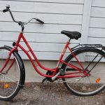 Punainen 28 -tuumainen Hilma Xtreme -merkkinen matalarunkoinen kaupunkipyörä. Pyörässä on useita heijastimia, valkoinen seisontatuki, tarakka, soittokello.